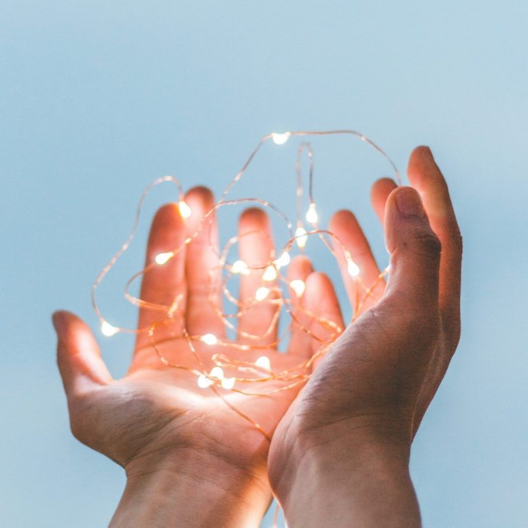 Two hands holding delicate fairy lights against a soft blue background.