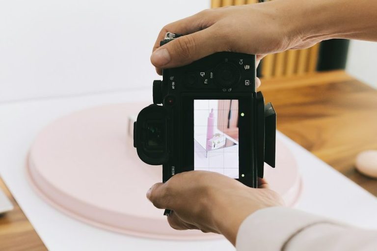 A person holding a camera, capturing a product on a pink display stand.
