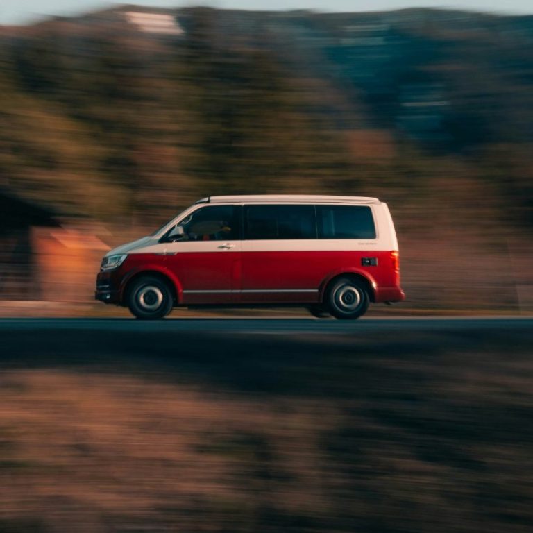 A light blue van driving on a road surrounded by green grass.